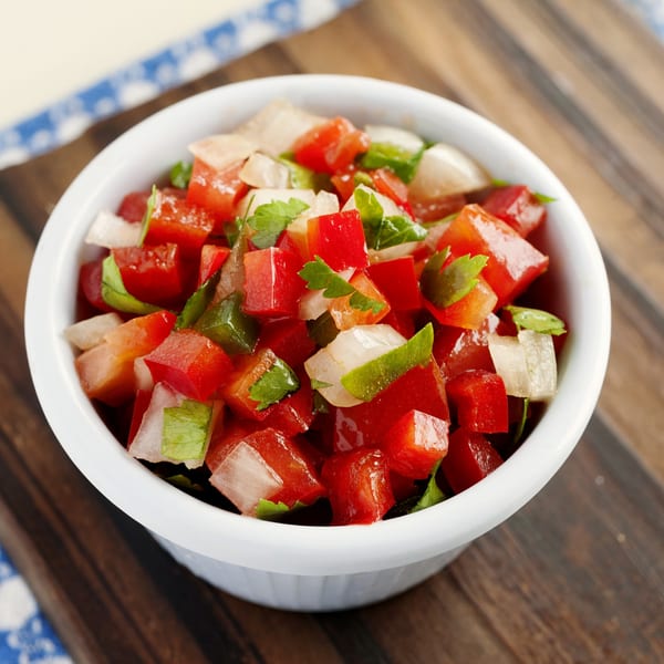 Freshly diced pico de gallo with tomatoes, onions, and cilantro in a white bowl on a wooden board.