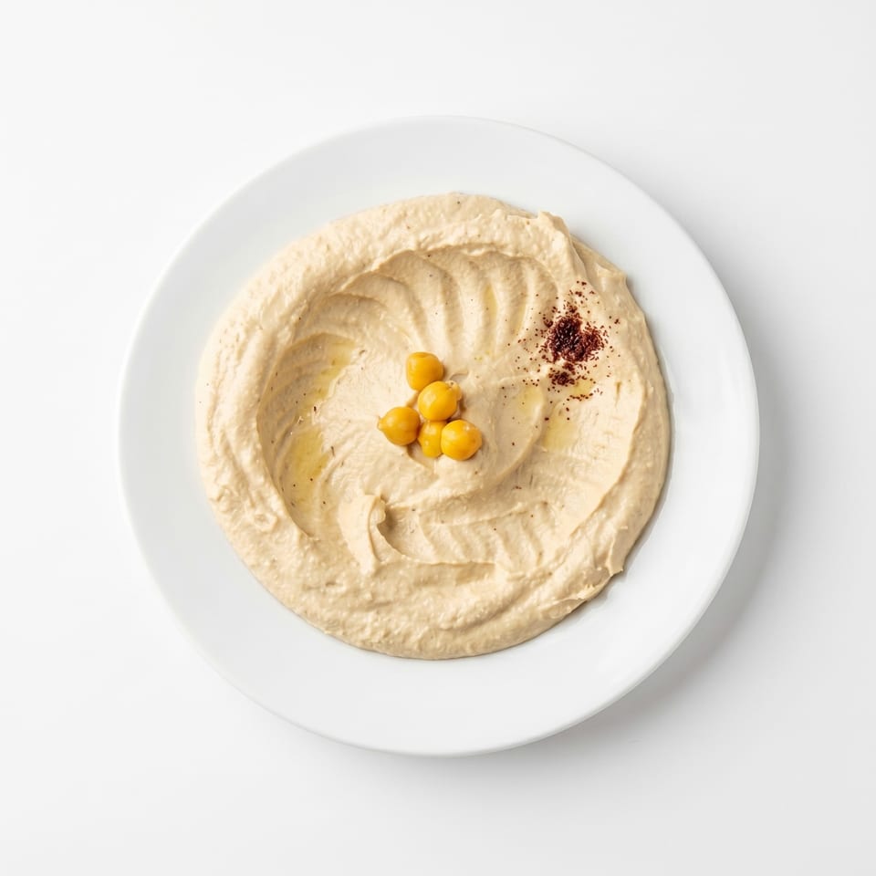 Creamy hummus swirled on a white plate, garnished with whole chickpeas and a sprinkle of paprika.
